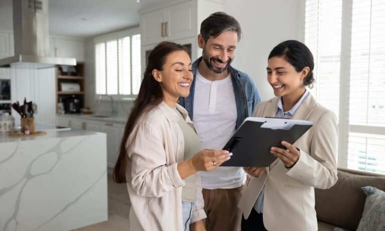 A first-time buyer couple reviews property details with an estate agent inside a modern home, illustrating the home-buying process discussed in the Swansea first-time buyer guide for 2026.