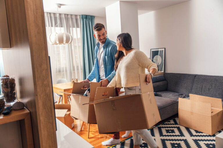 Couple carrying moving boxes into their new rental home, representing tenants relocating to Burton or Somerford in Christchurch.